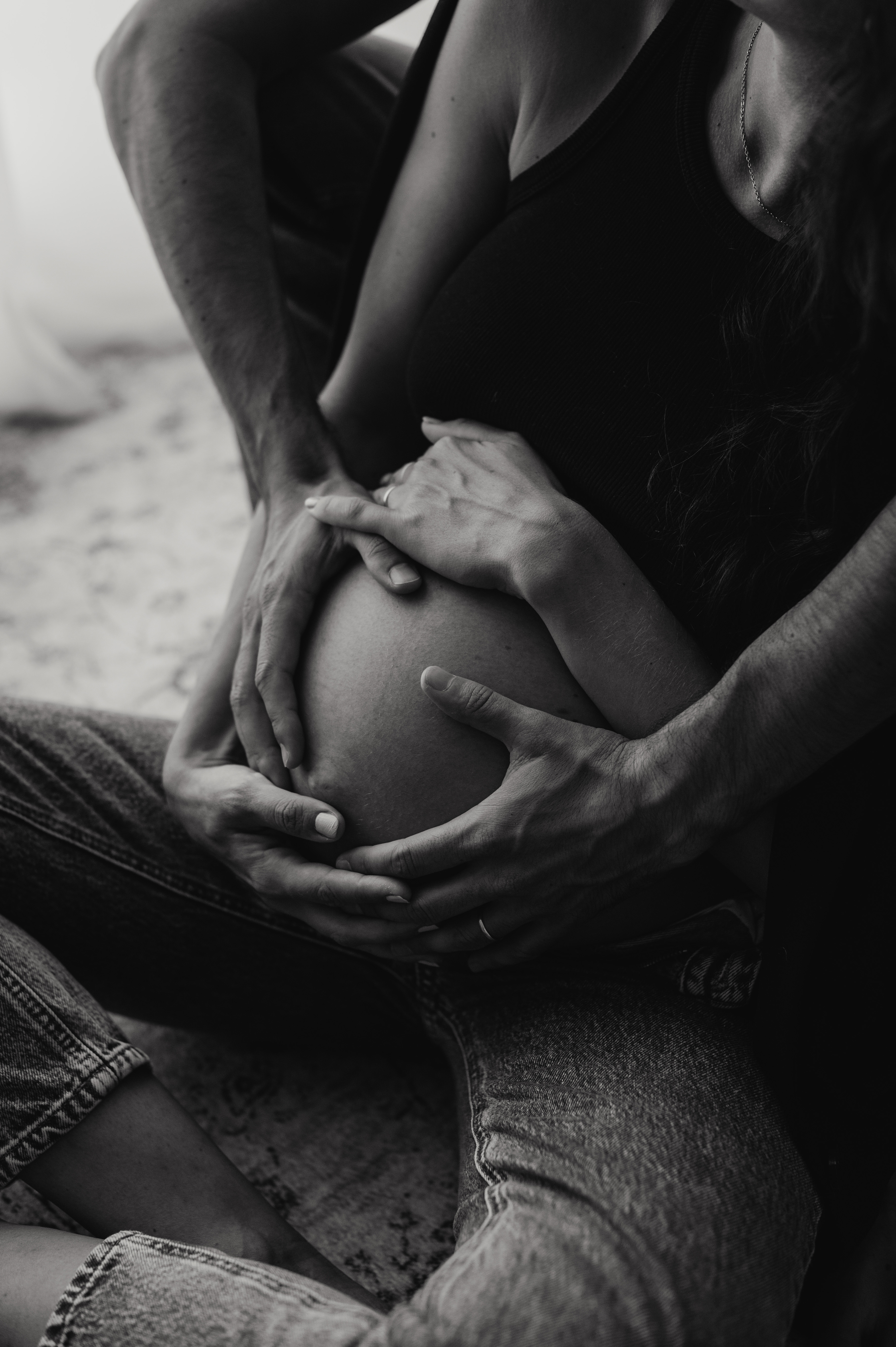 Dettaglio maternity in bianco e nero: le mani della coppia appoggiate insieme sul pancione