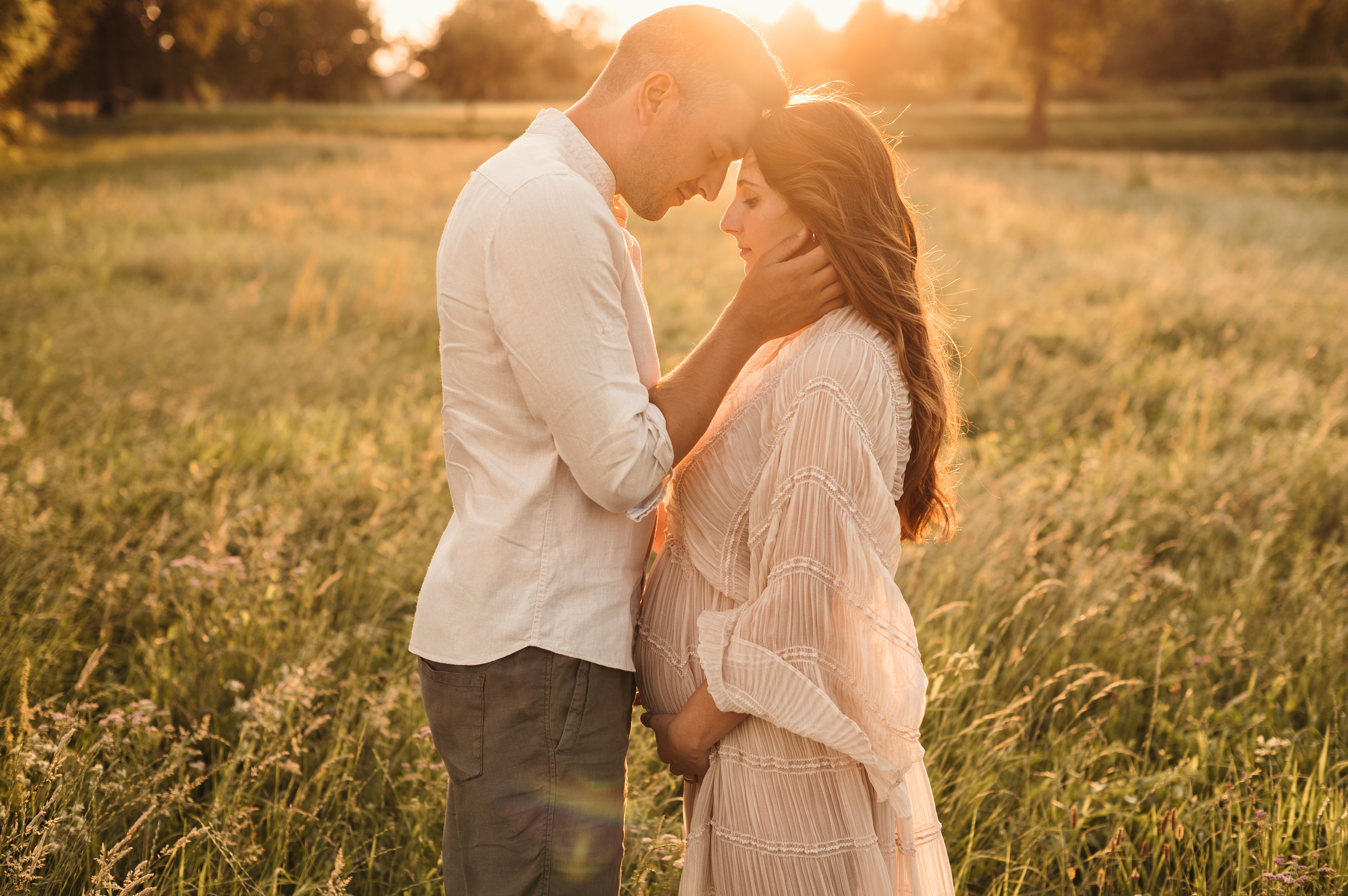 Sessione maternity in esterna al tramonto: coppia fronte a fronte con le mani sul pancione