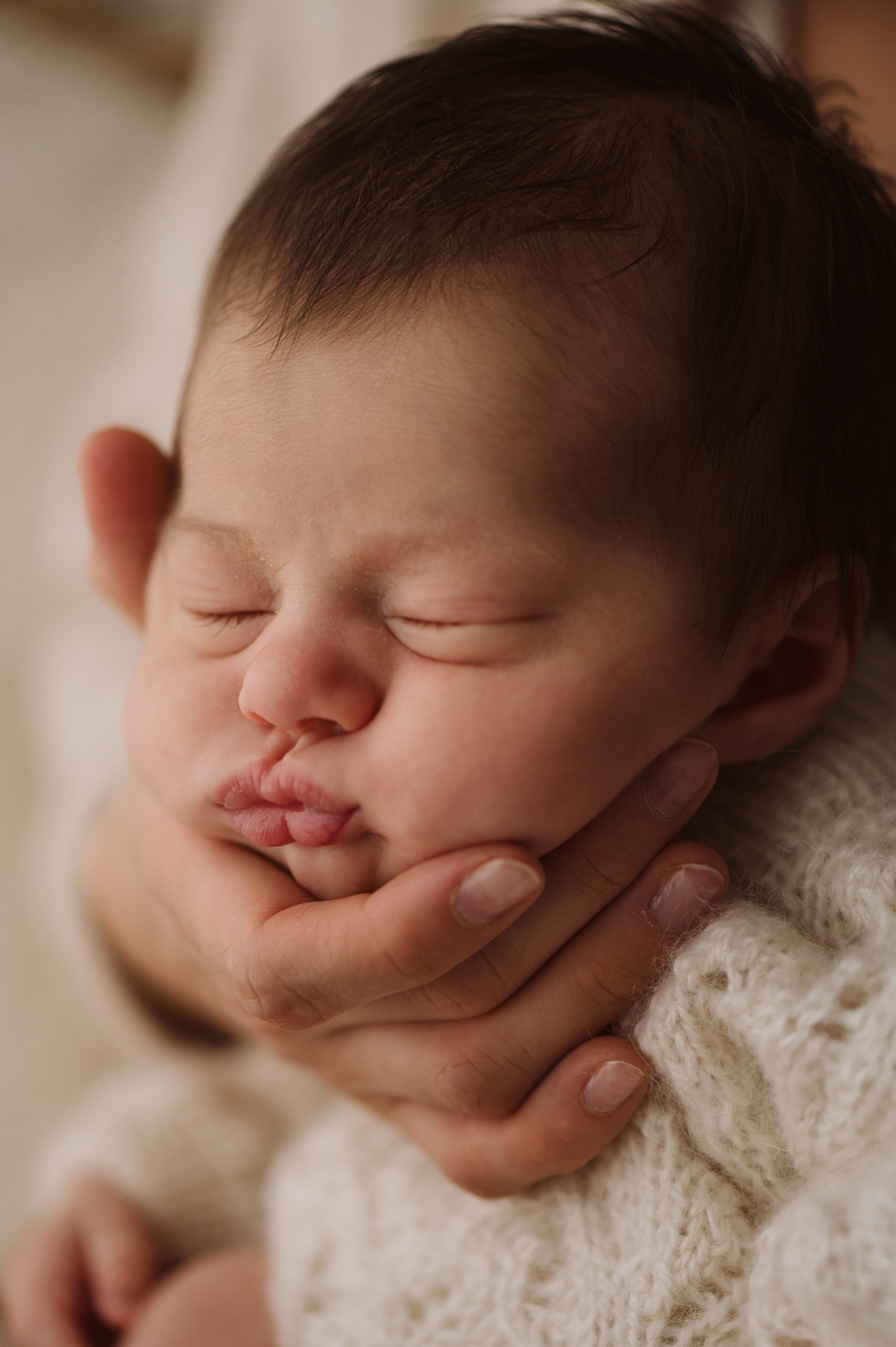Primo piano del viso di un neonato che dorme appoggiato alla mano di un genitore