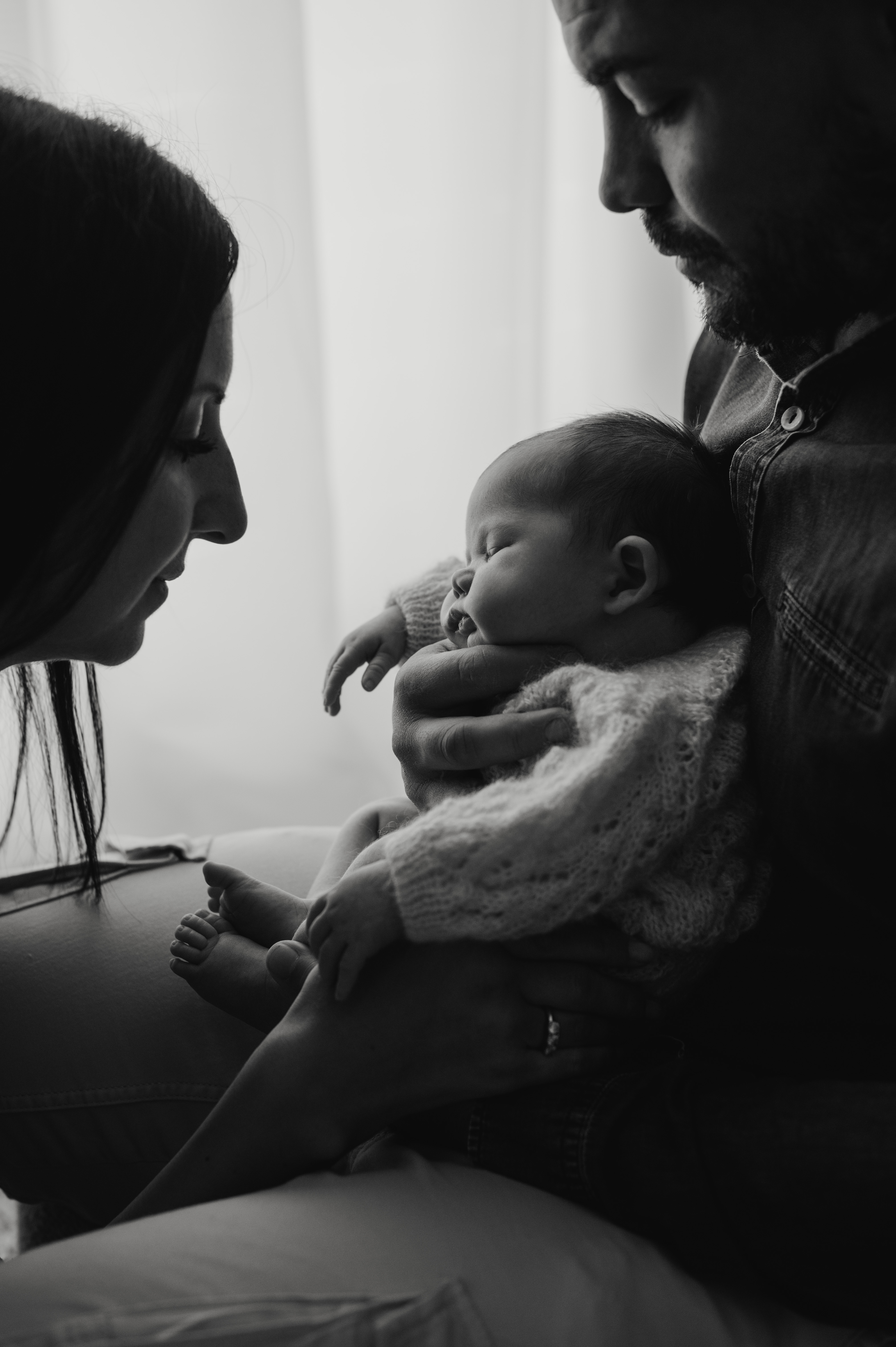 Servizio newborn in studio in bianco e nero: neonato in braccio al papà, con la mamma che lo guarda