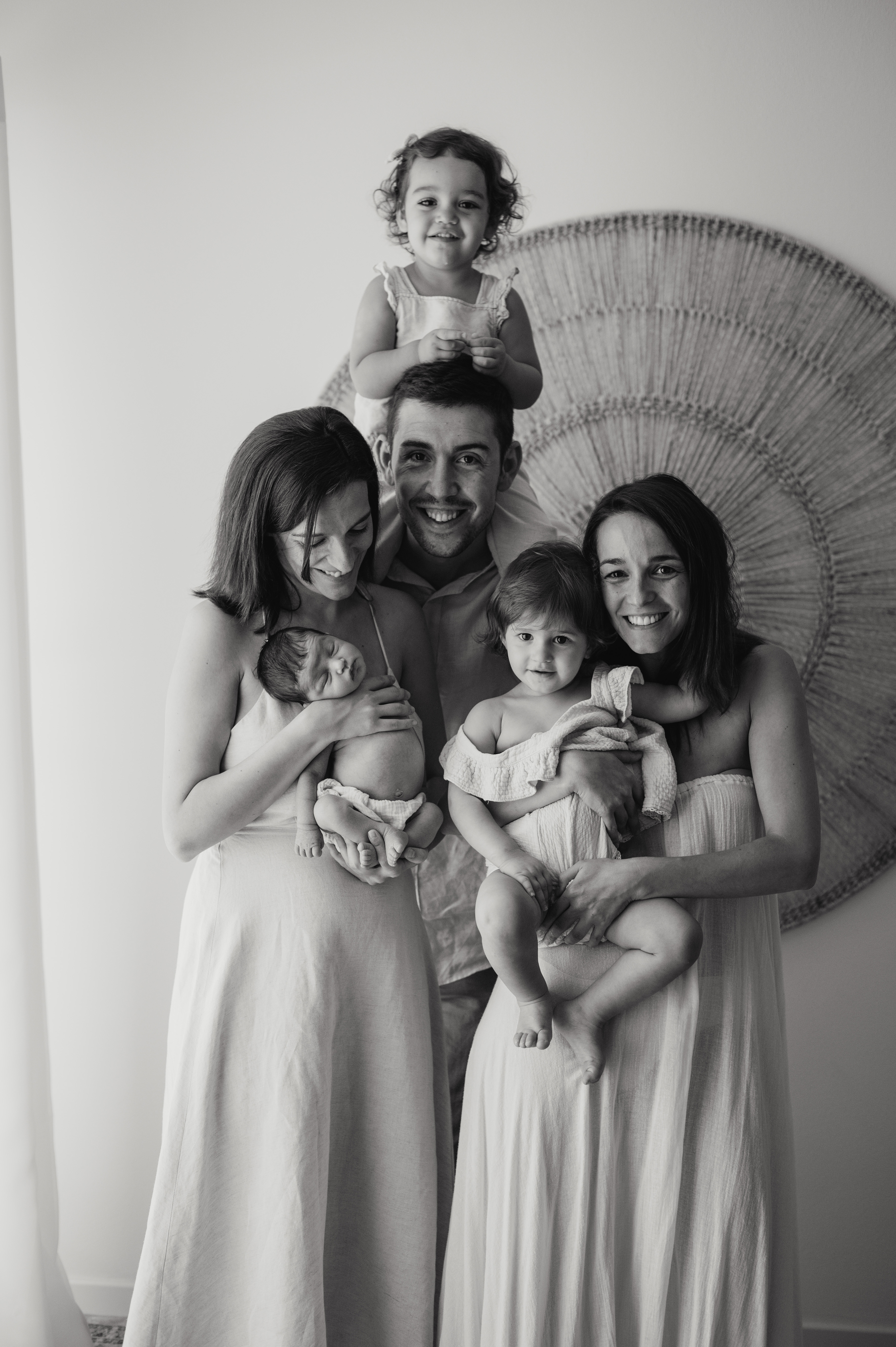 Ritratto di famiglia in bianco e nero durante la sessione newborn: genitori con il neonato e tre bambini in studio