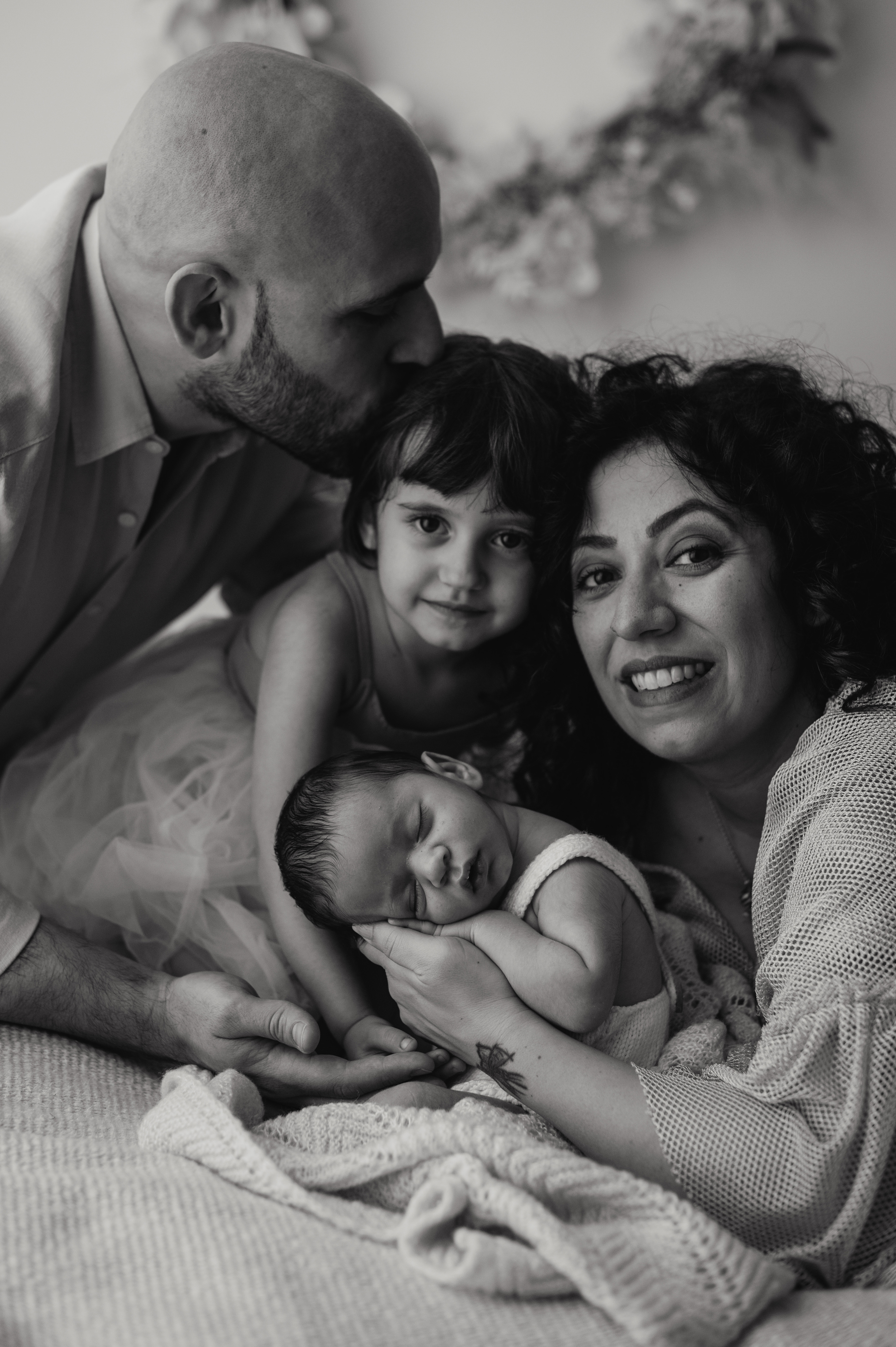 Ritratto di famiglia in bianco e nero: mamma, papà e sorellina intorno al neonato, sessione in studio
