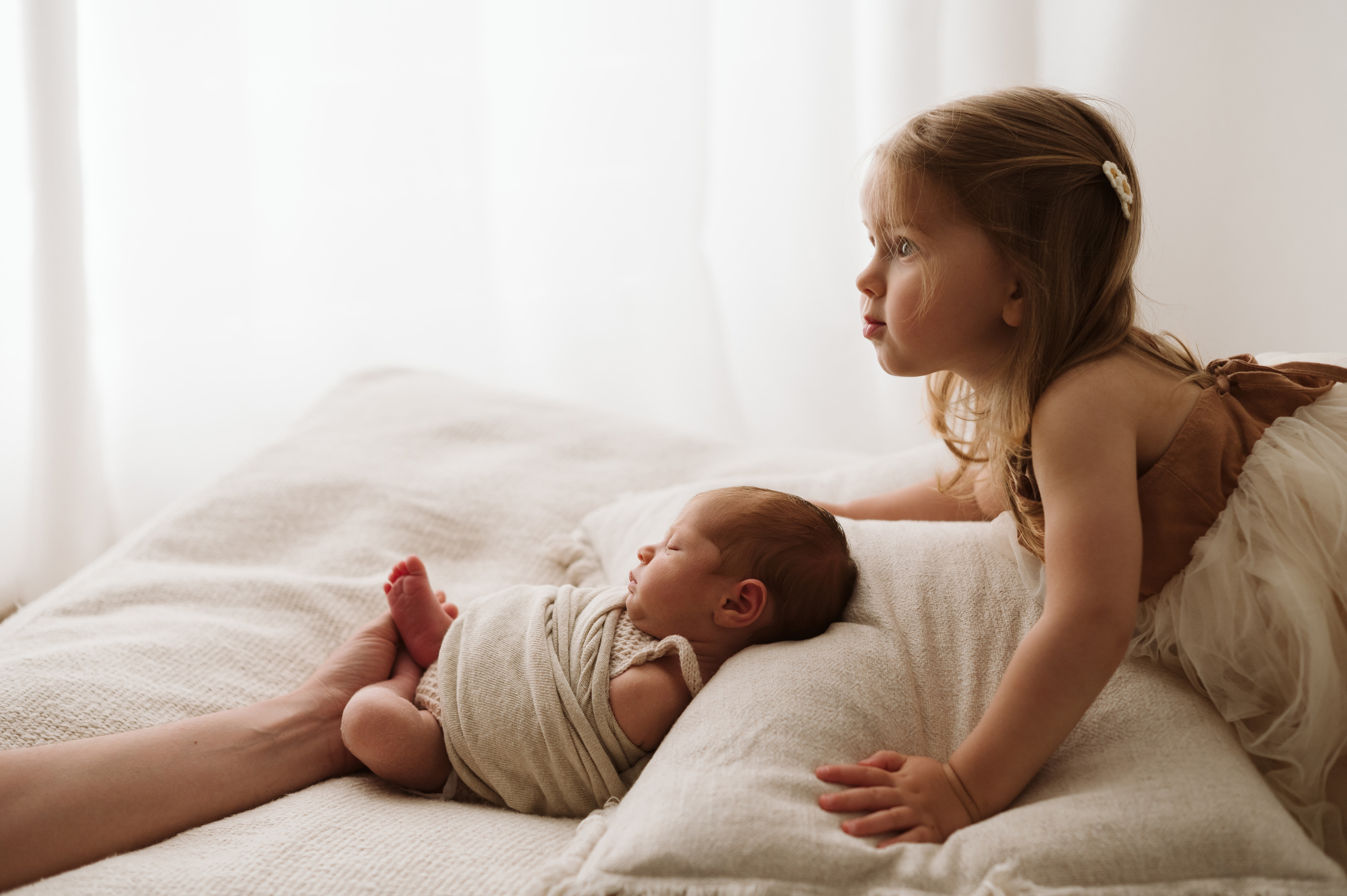 Sessione newborn in studio: neonato avvolto in una fascia sul letto accanto alla sorella maggiore