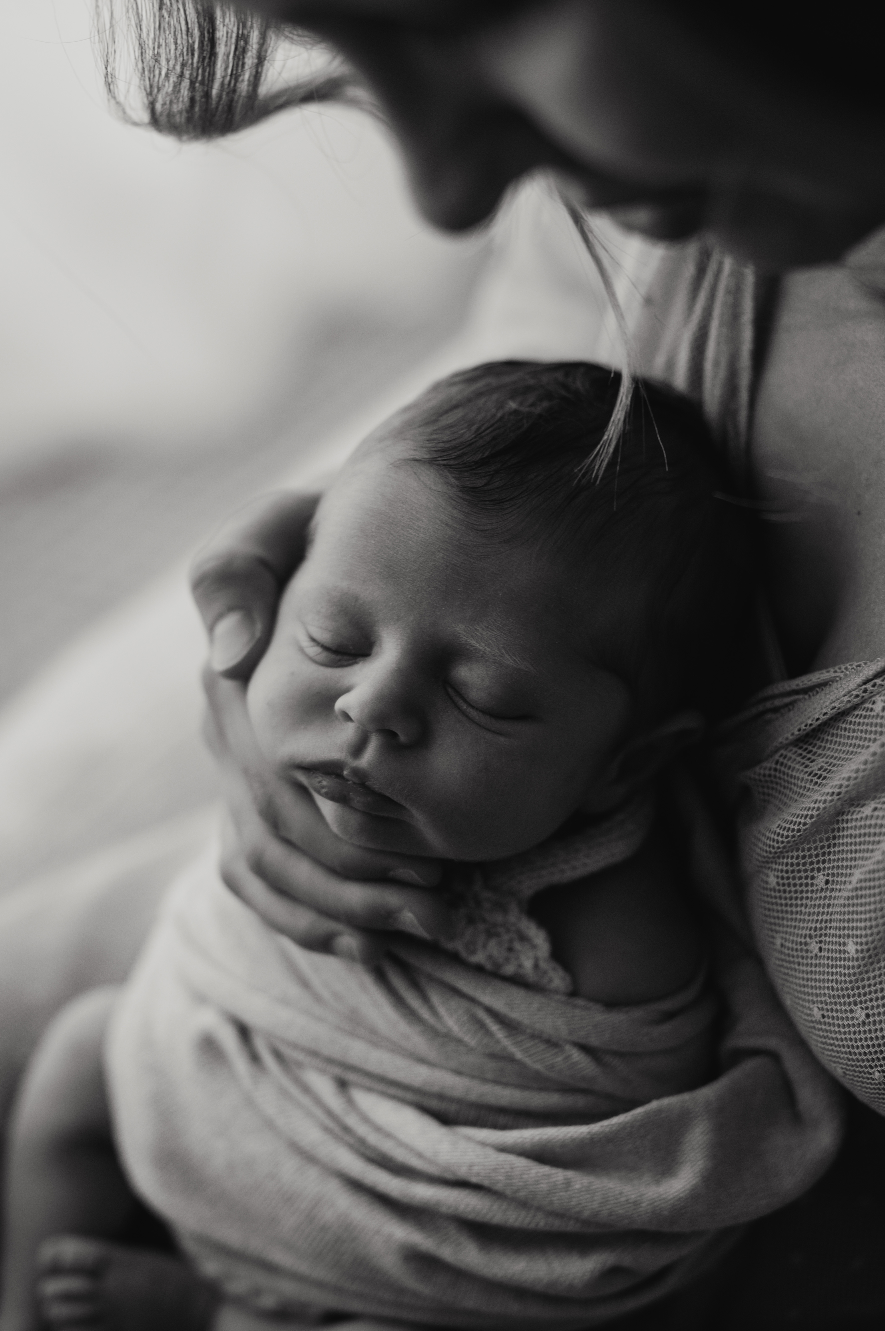 Servizio newborn in bianco e nero: neonato fasciato addormentato in braccio alla mamma