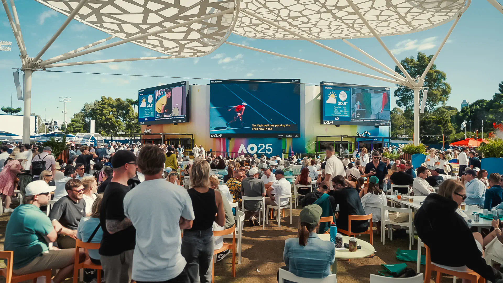 a group of people sitting at tables and chairs in front of a large screen