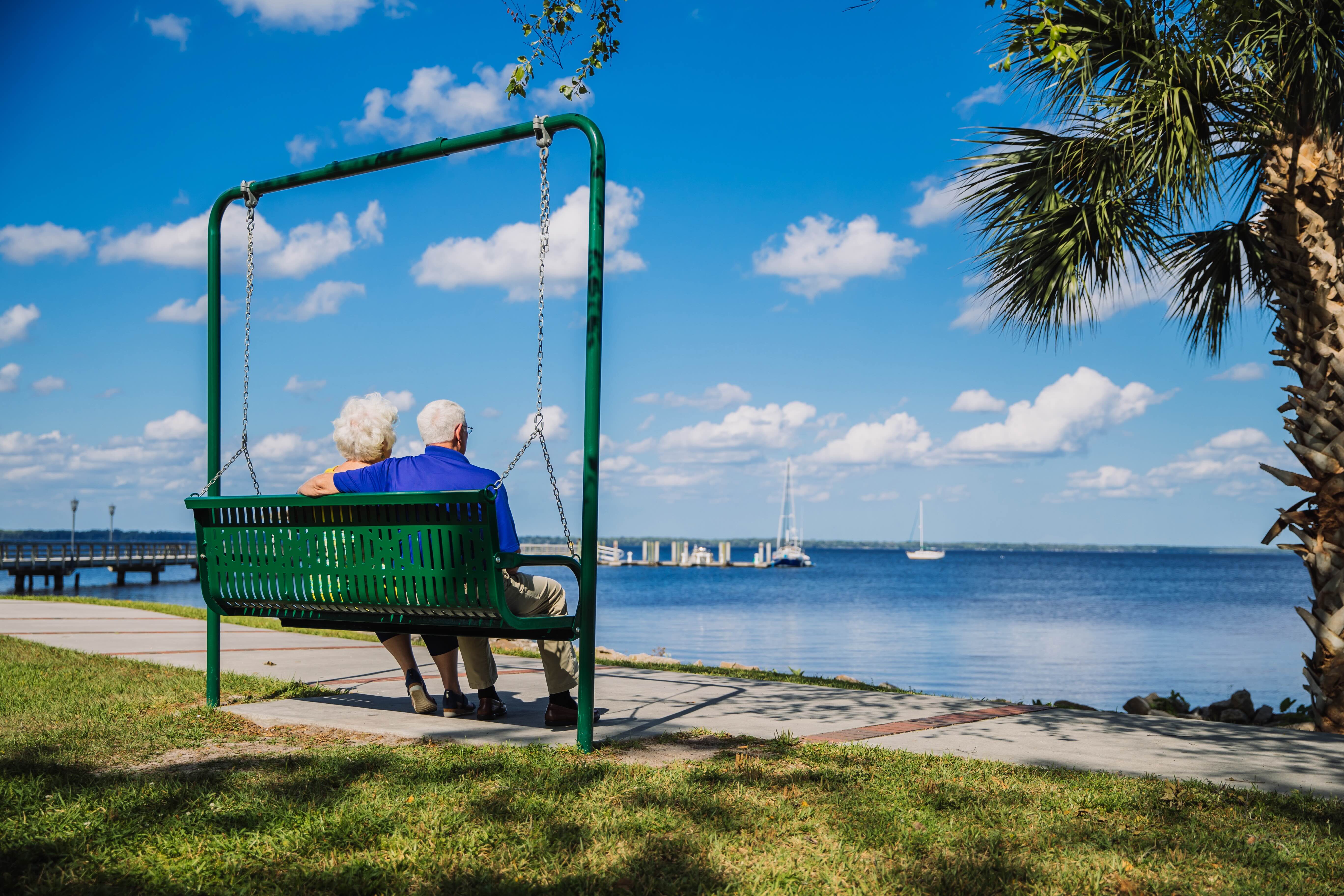 A man and a woman sitting on a swing by the water