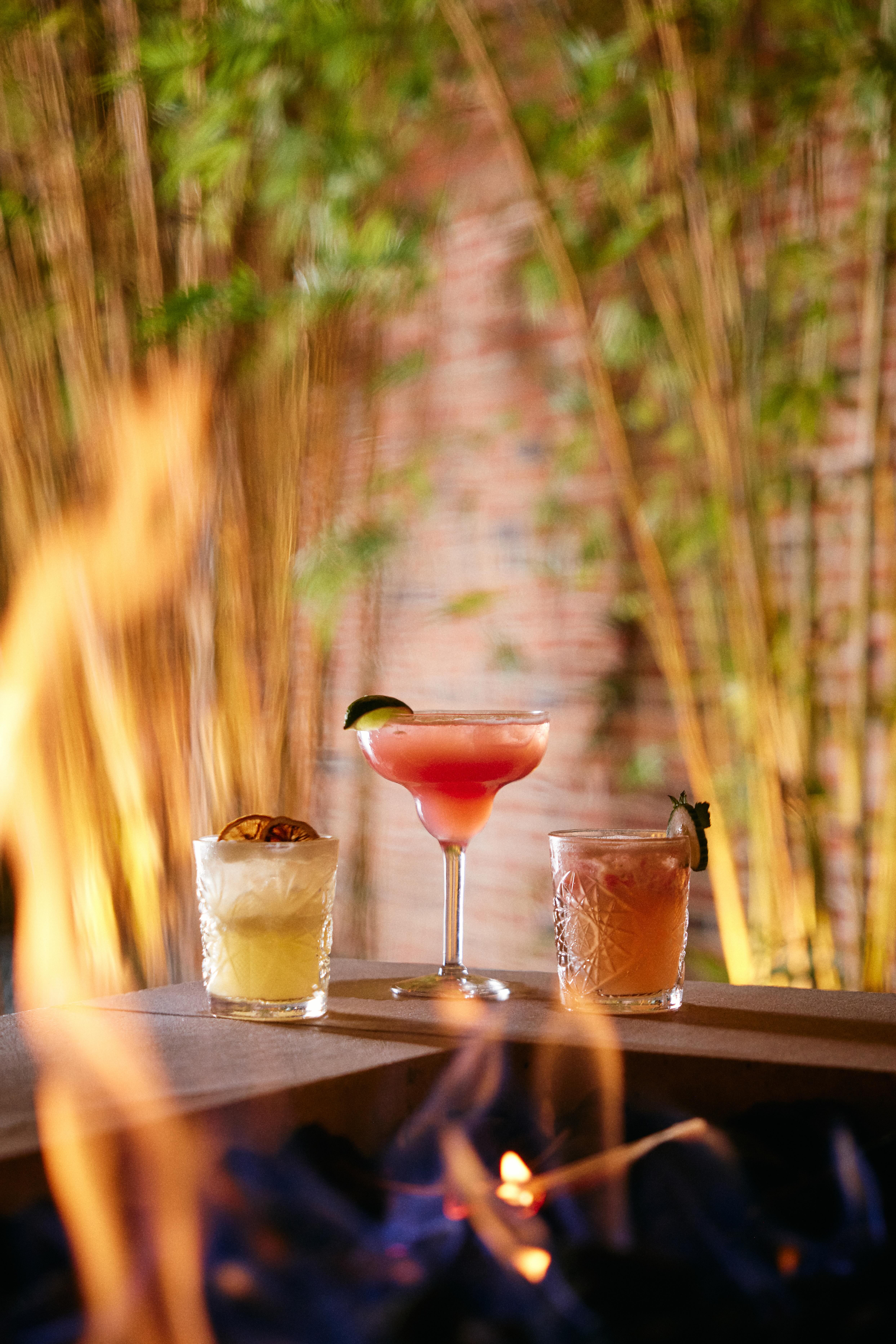 Three cocktails sitting on top of a table next to a fire