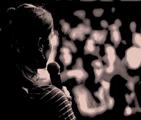 Silhouette of a person holding a microphone and speaking to a blurred audience.