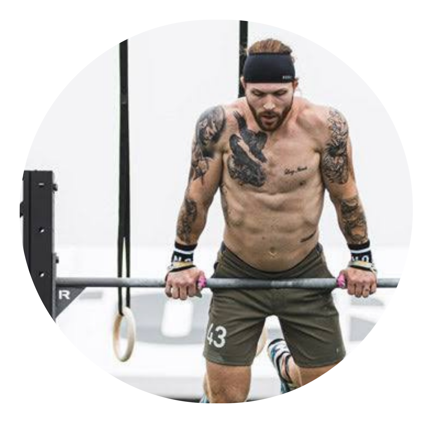 Tattooed shirtless man wearing a headband and wrist wraps performing a bar exercise at a gym.