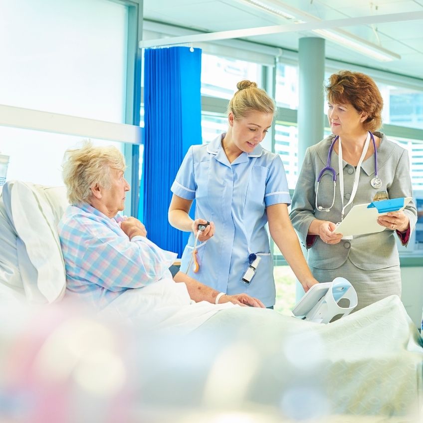 a female hospital nurse is checking the blood pressure of an elderly women laying on a hospital bed.