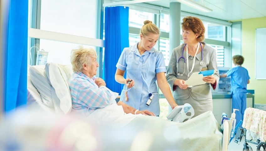 a female hospital nurse is checking the blood pressure of an elderly women laying on a hospital bed.