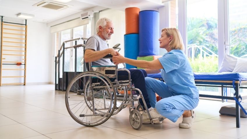 Senior Man in Wheelchair Receiving Assistance from Physiotherapy Nurse