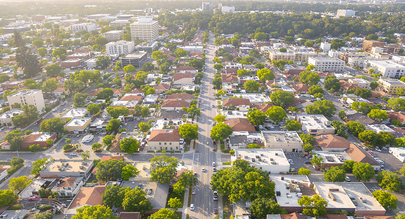 Aerial view of vibrant Sun Belt city neighborhood with mixed housing and busy streets under warm light.