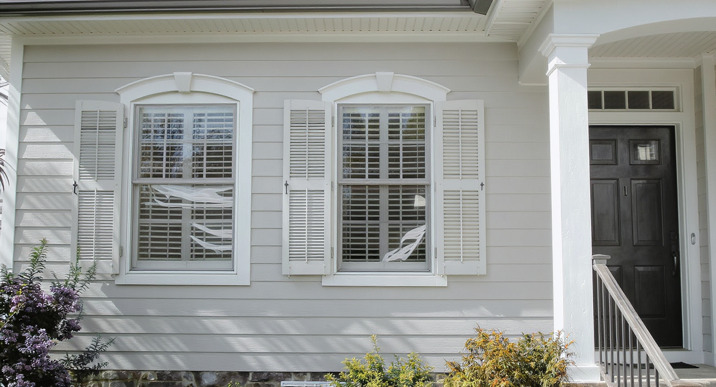 House facade with perfectly sized shutters, neutral siding and trim, low portico, and soft foundation plants under balanced daylight.