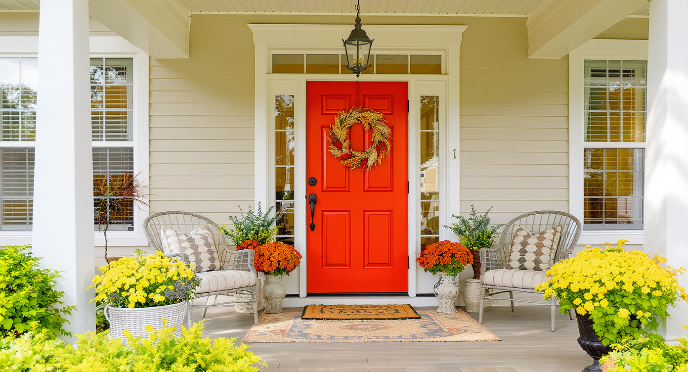 A bright front porch featuring a bold colored door, stylish furniture, and vibrant plants, inviting warmth and charm.