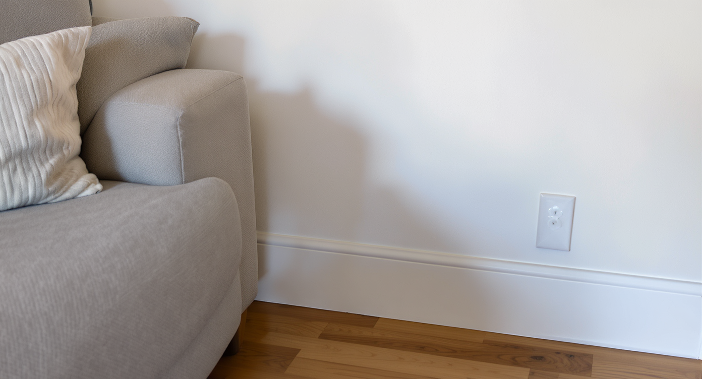Empty living room corner with blank white wall and sofa, showing missing decor elements that affect room scale perception.