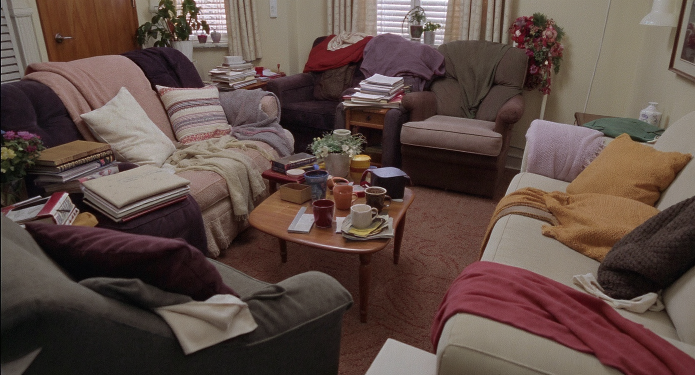 Overcrowded small living room with multiple pieces of furniture and clutter making space feel cramped.