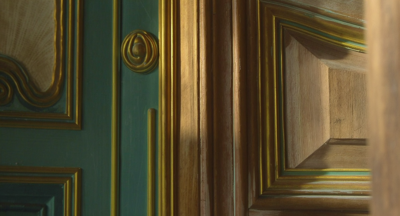 Intricate wood paneling and moldings in teal and gold in a historic home, showcasing vibrant architectural details.