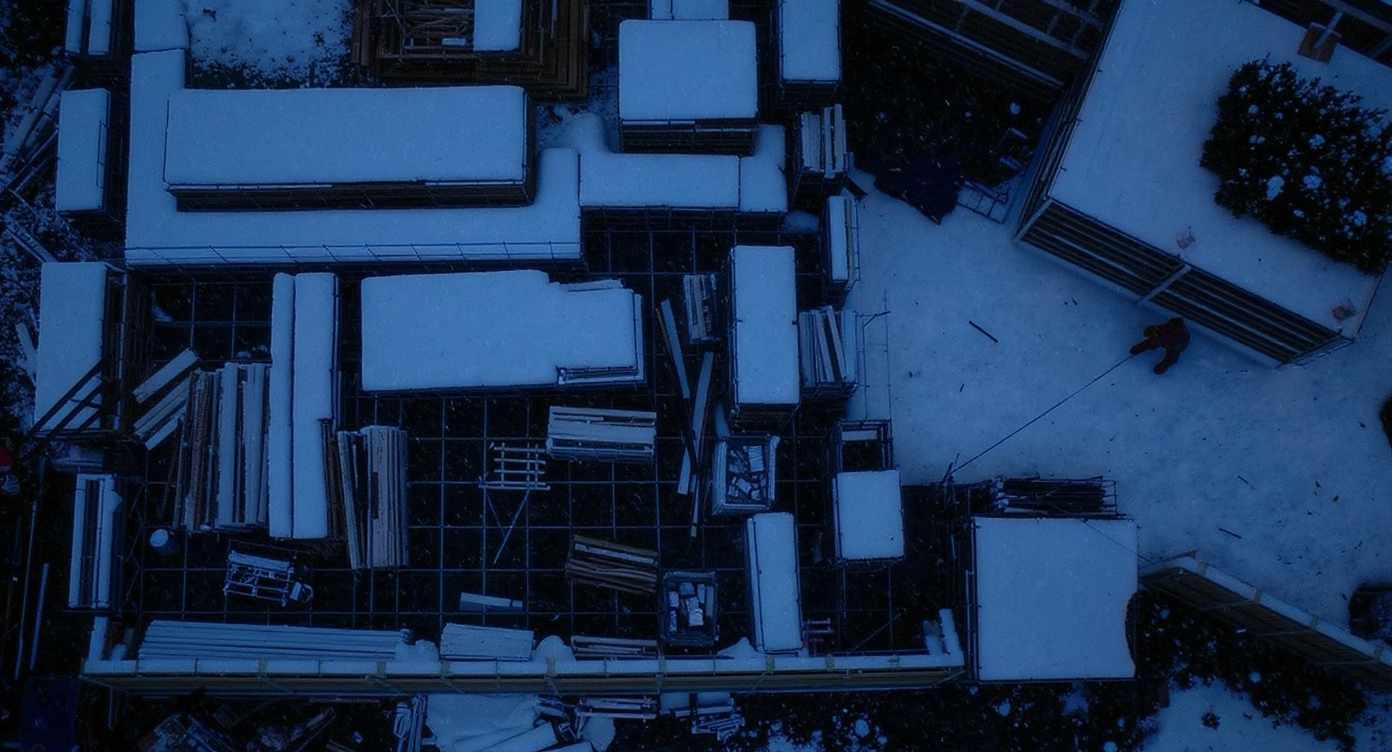 A construction site being prepared for snowfall, with secured materials and falling snow.
