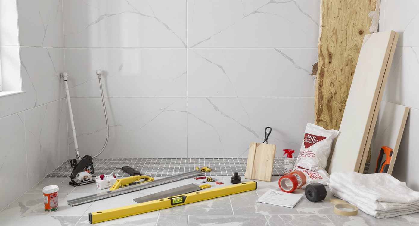 Modern bathroom mid-renovation, with partially tiled shower, tiling and plumbing tools, and materials arranged for a realistic DIY workspace.
