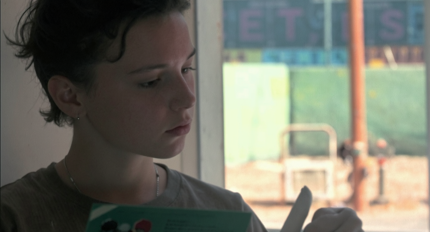 Three sections of plywood climbing wall panel rest on sawhorses, partially treated with paint, sealant, and patterns. Sanding and finishing tools also shown.