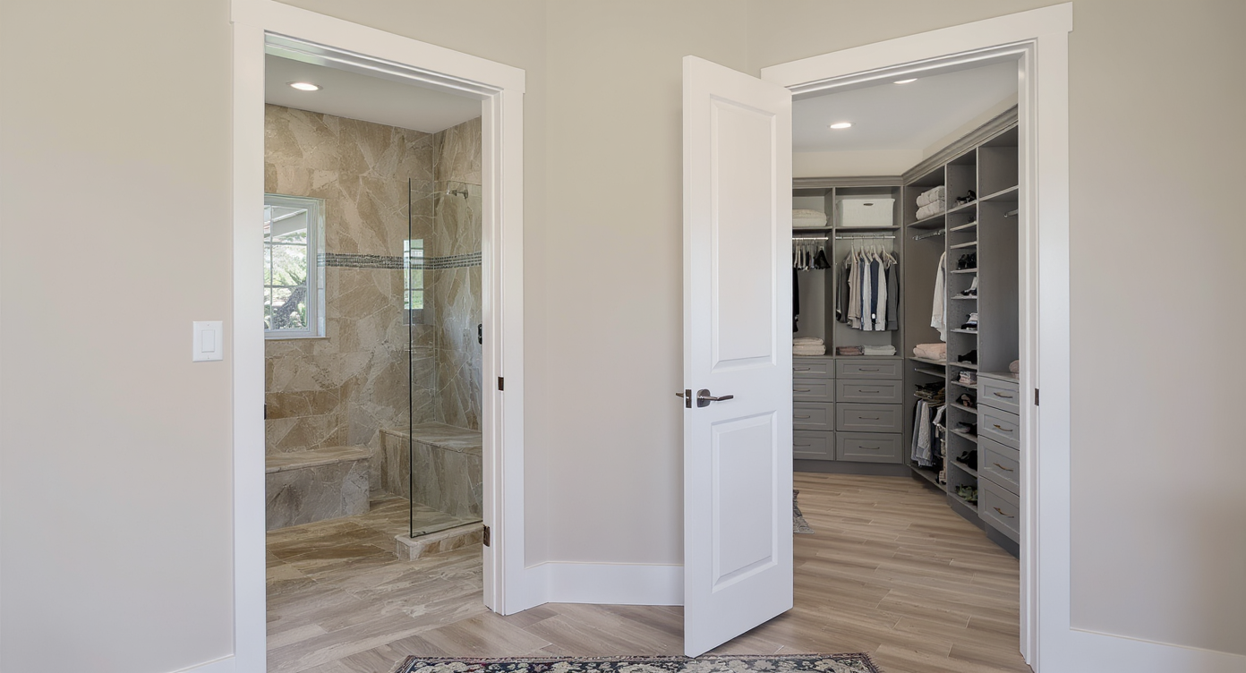 A modern primary suite showing a direct connection between a spa-like bathroom and a large walk-in closet with custom storage, no people.