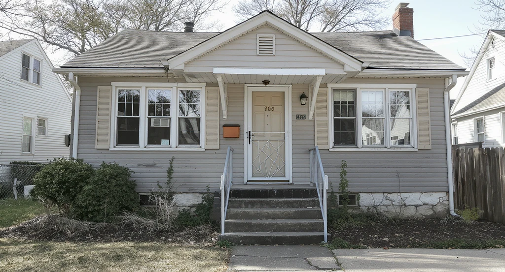 An unappealing house exterior with mismatched windows, missing shutters, neglected foundation landscaping, and awkward entry steps, illustrating how to make an ugly house exterior cute with affordable curb appeal makeover ideas and best exterior color combinations for resale.