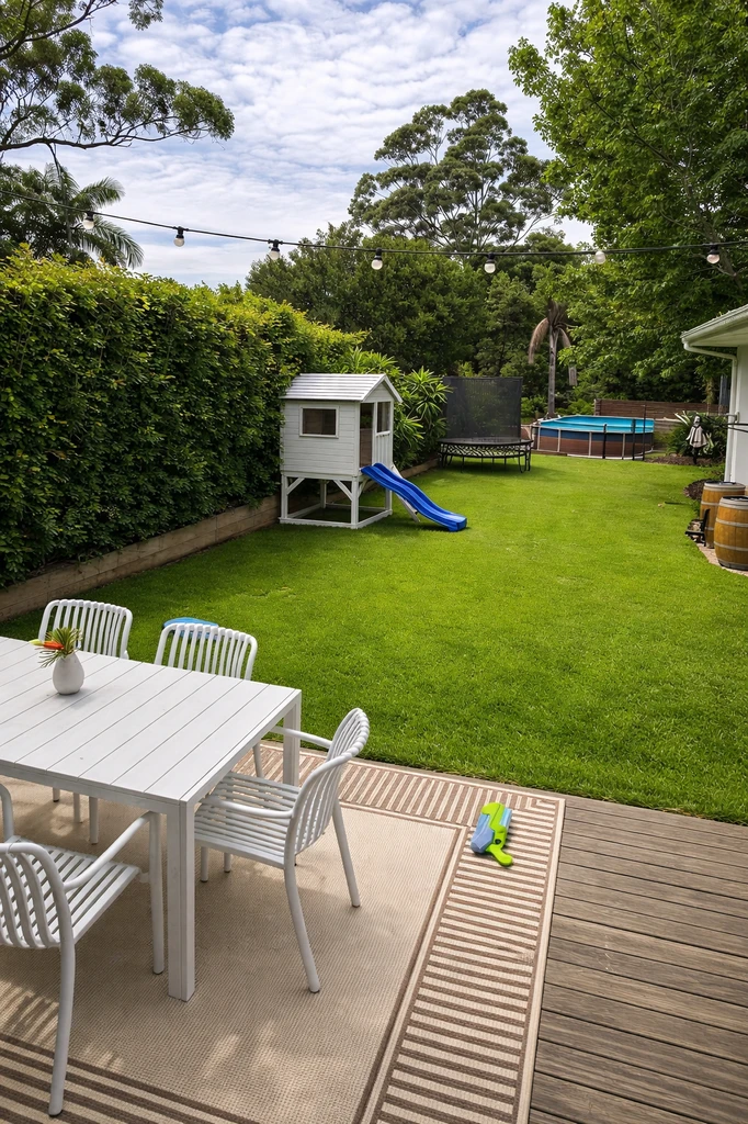 Large backyard with green lawn, soccer goal in the center, and a modern trampoline tucked snugly into the far back-left corner by the fence, optimizing space.
