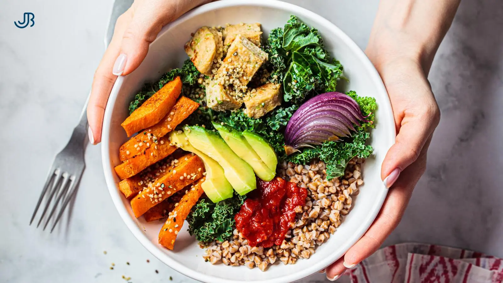 Gesunde Bowl mit gebackenen Süßkartoffeln, Avocado, Grünkohl, roten Zwiebeln, Hähnchenstücken, Buchweizen und einem Klecks Tomatensoße. Die farbenfrohe Mahlzeit symbolisiert ausgewogene Ernährung und gesunde Essgewohnheiten.