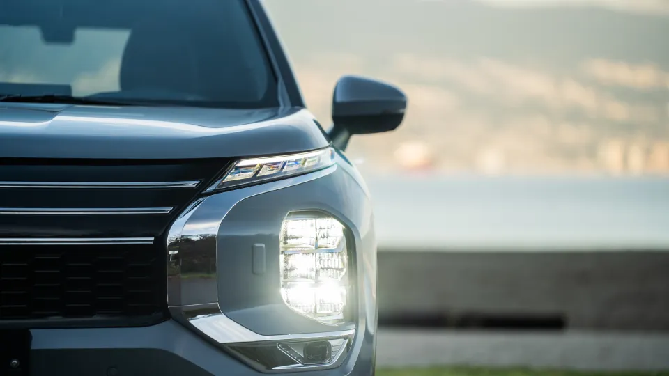 Close-up of a car's front right headlight and side mirror with a blurred background.