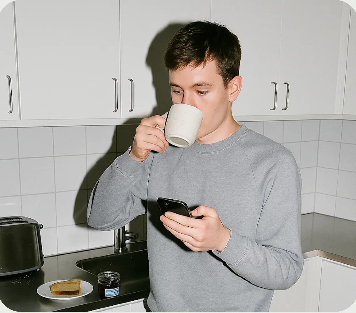 Un hombre tomando una taza de café mientras sostiene un teléfono celular.