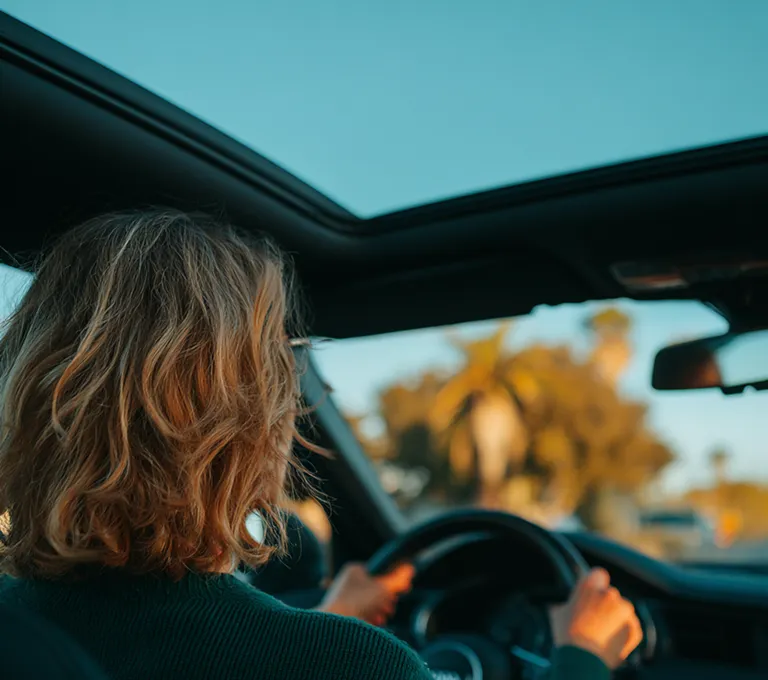 Uma mulher dirigindo um carro em um dia ensolarado.