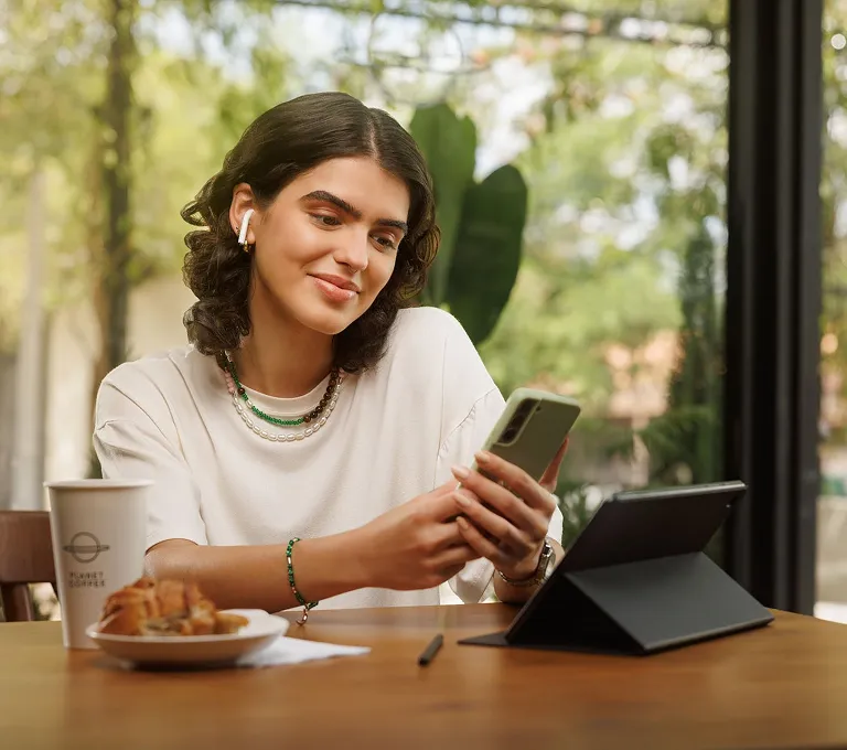 Uma mulher sentada à mesa olhando para o celular.