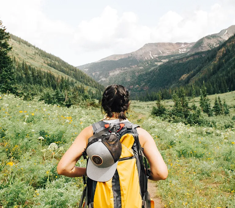 Uma mulher com uma mochila caminhando por um campo de flores silvestres.