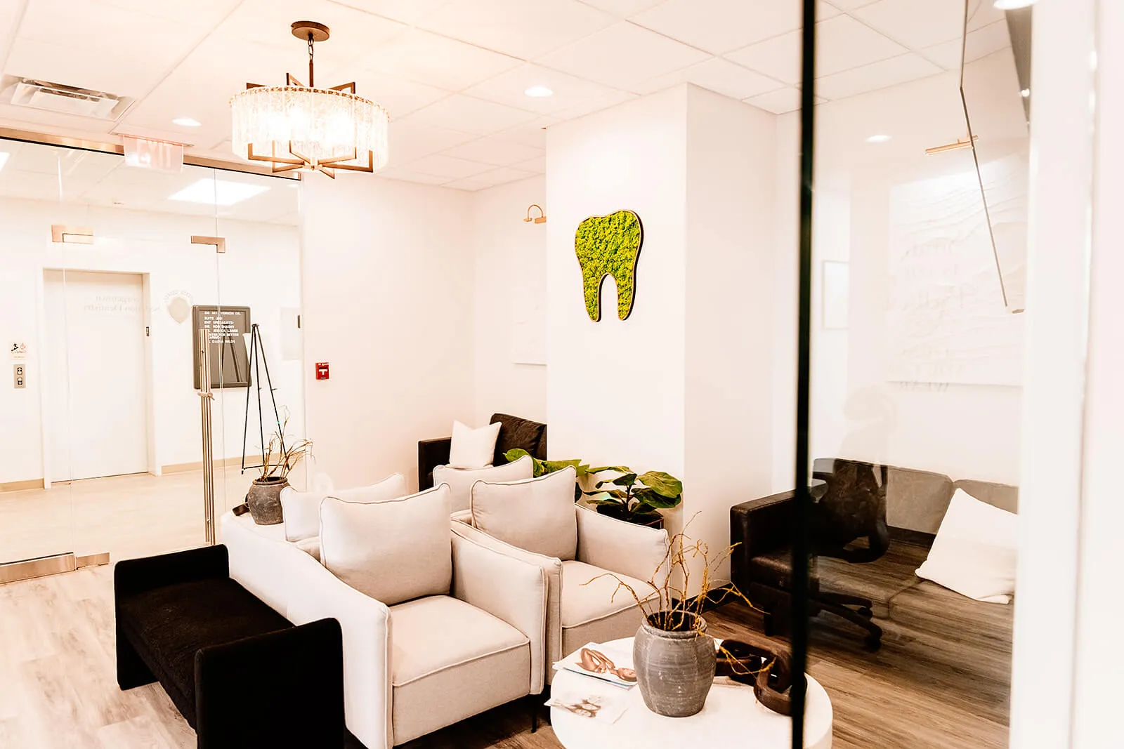 Modern dental office waiting room with white sofas, green tooth artwork on wall, and elegant lighting.