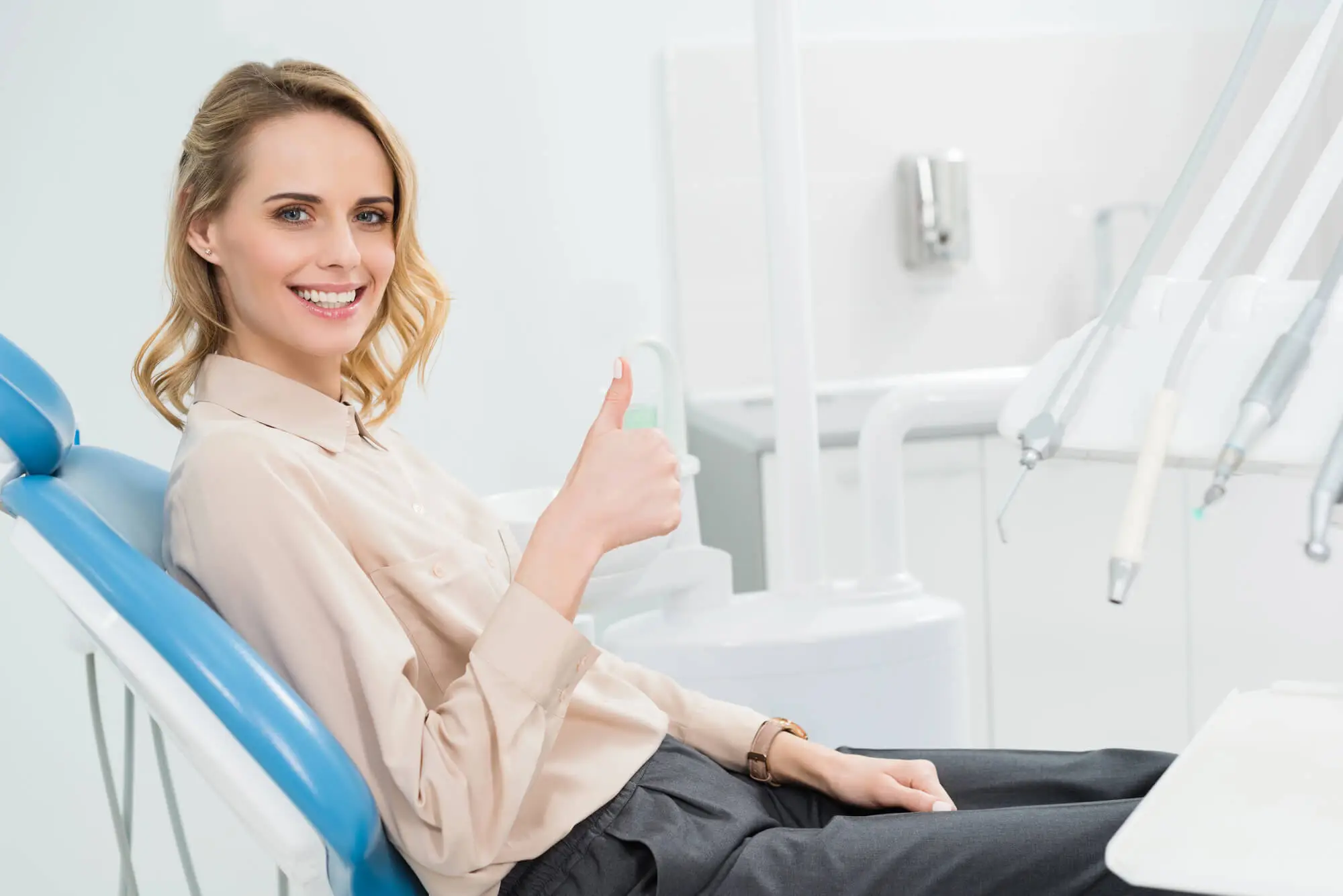 Close-up of a woman smiling with eyes closed during a dental checkup, a dentist's gloved hand holding a dental mirror near her teeth