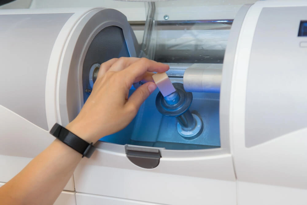 Person's hand placing a dental milling block into a modern white dental milling machine