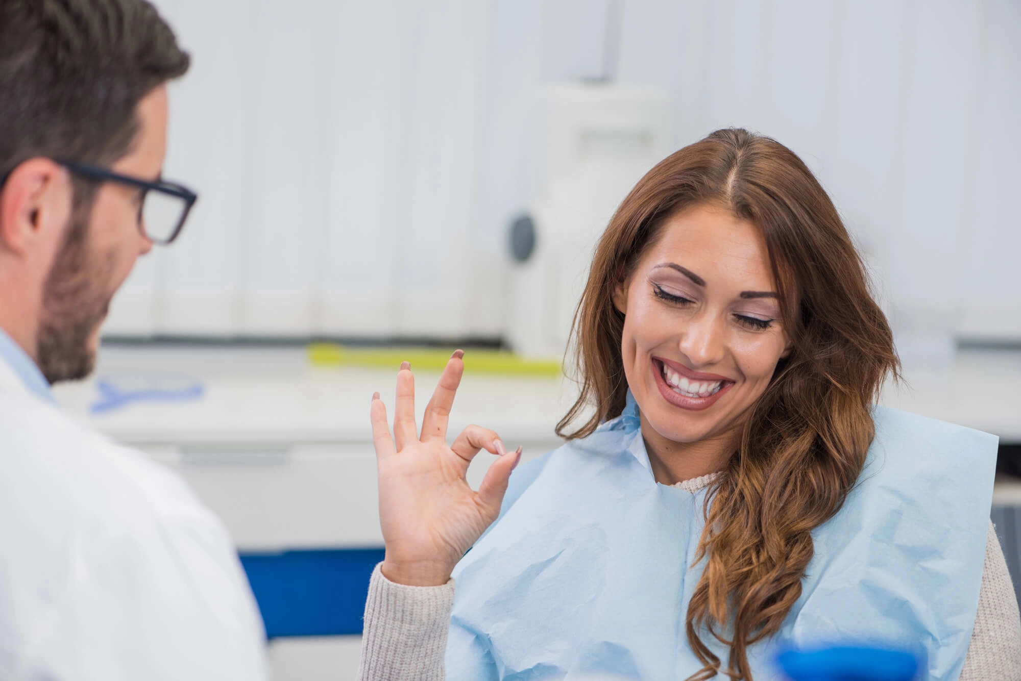 Patient in dental chair giving an OK hand gesture to a dentist in a clinical setting