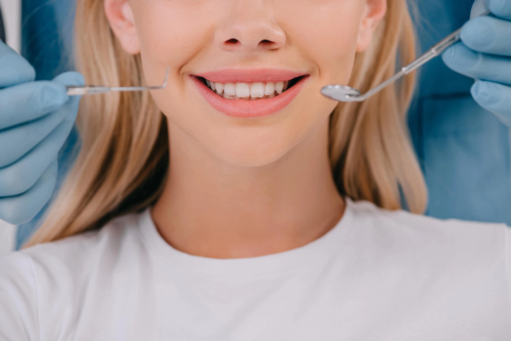 Smiling woman during dental check-up with dentist's gloved hands holding probes near her mouth; evokes a sense of relaxation and care