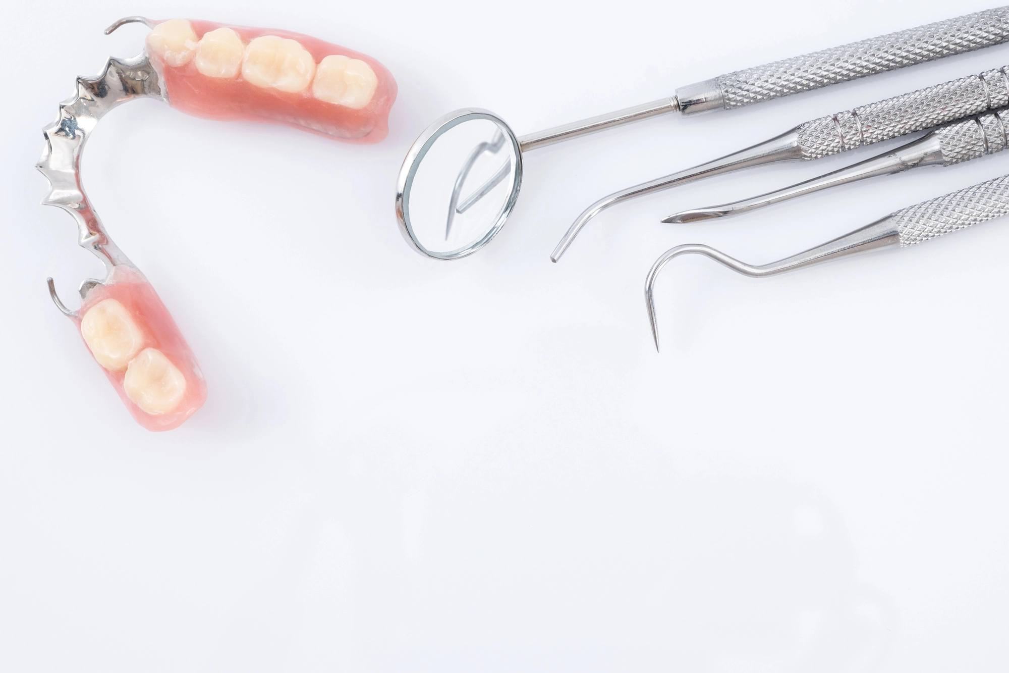 Partial dentures and three stainless steel dental tools including a mirror on a white background