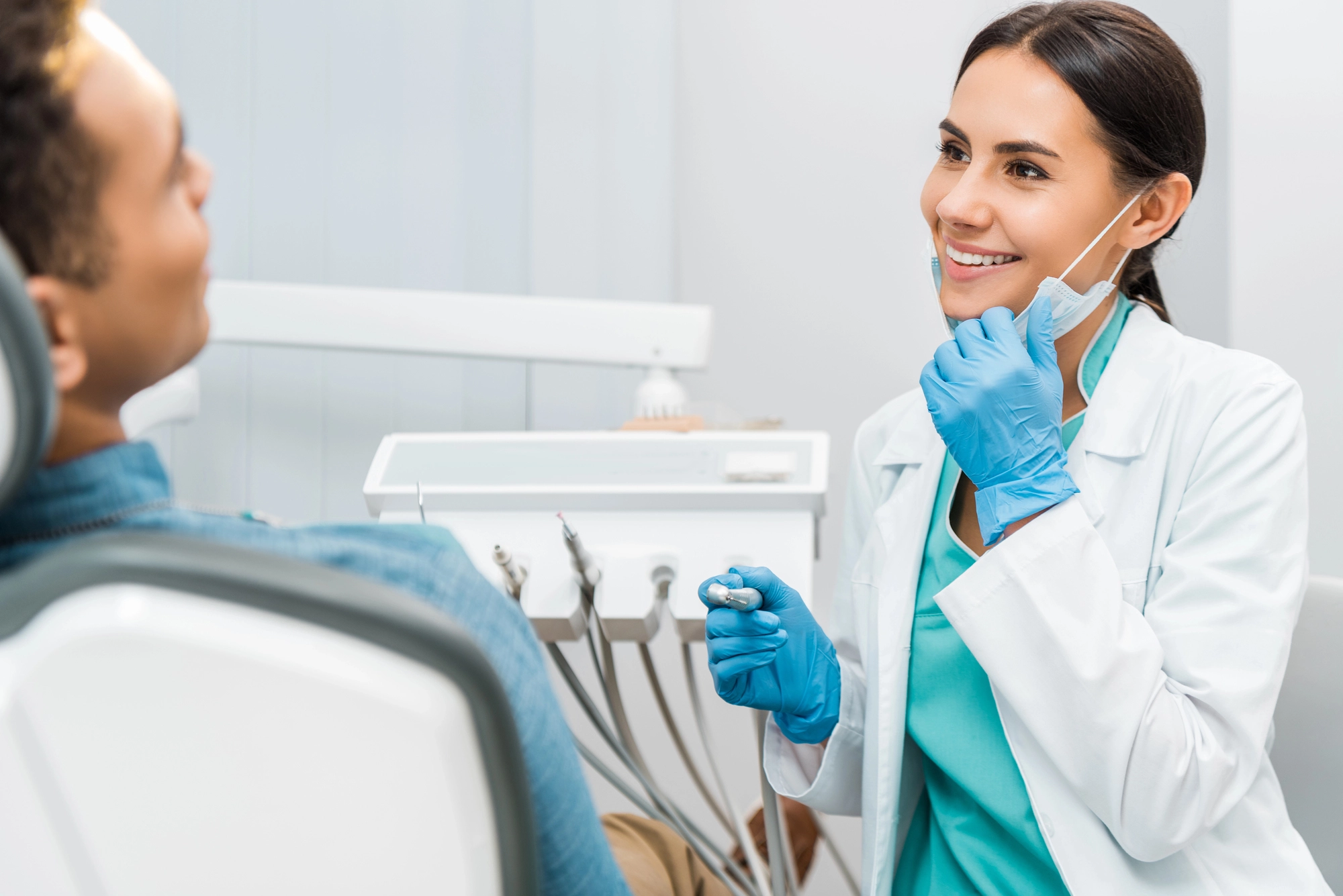 Dentist wearing gloves preparing dental tools while talking to a patient seated in a dental chair in a clinic