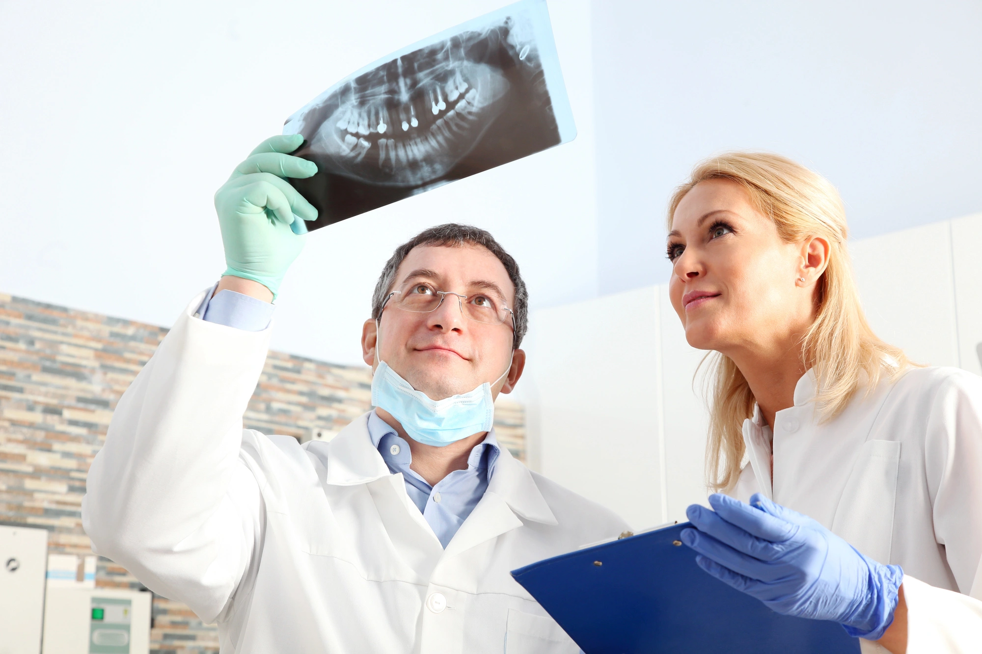 Two dentists in lab coats examining a dental X-ray while discussing patient information on a clipboard in a clinic