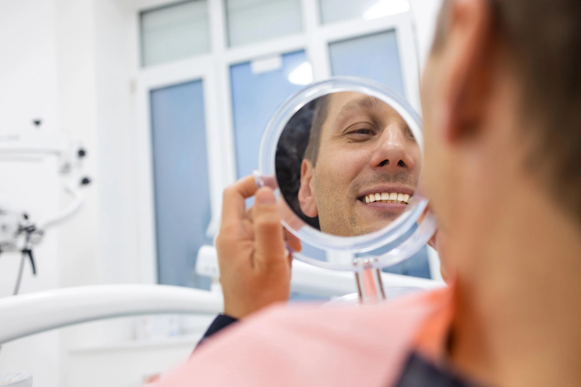 Patient checking his smile in a mirror after visiting a dentist in Georgetown, KY