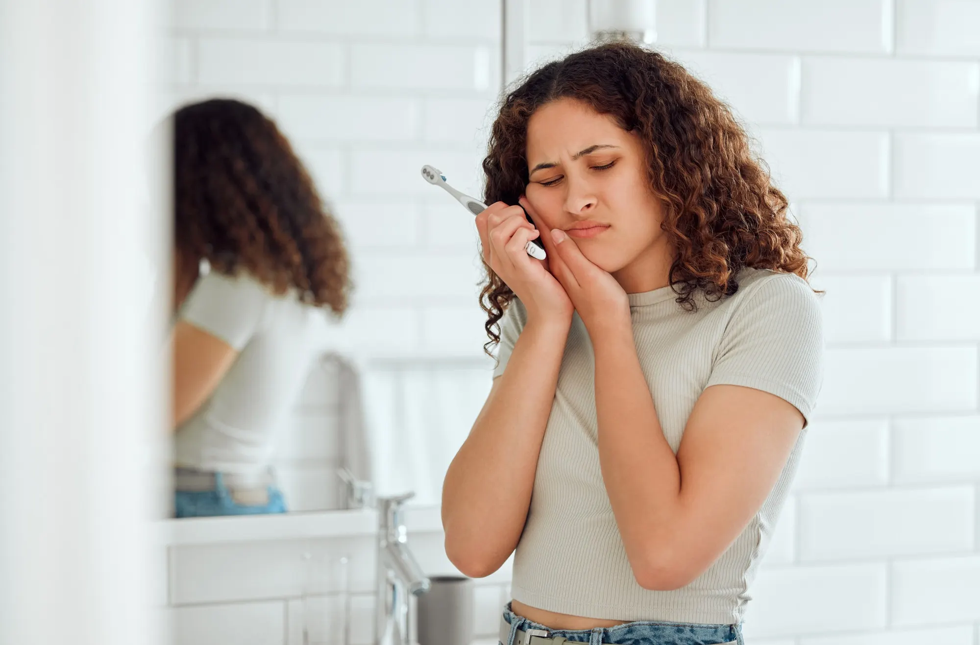 Woman experiencing tooth pain while holding an electric toothbrush, suggesting the need for an emergency dentist in Lexington