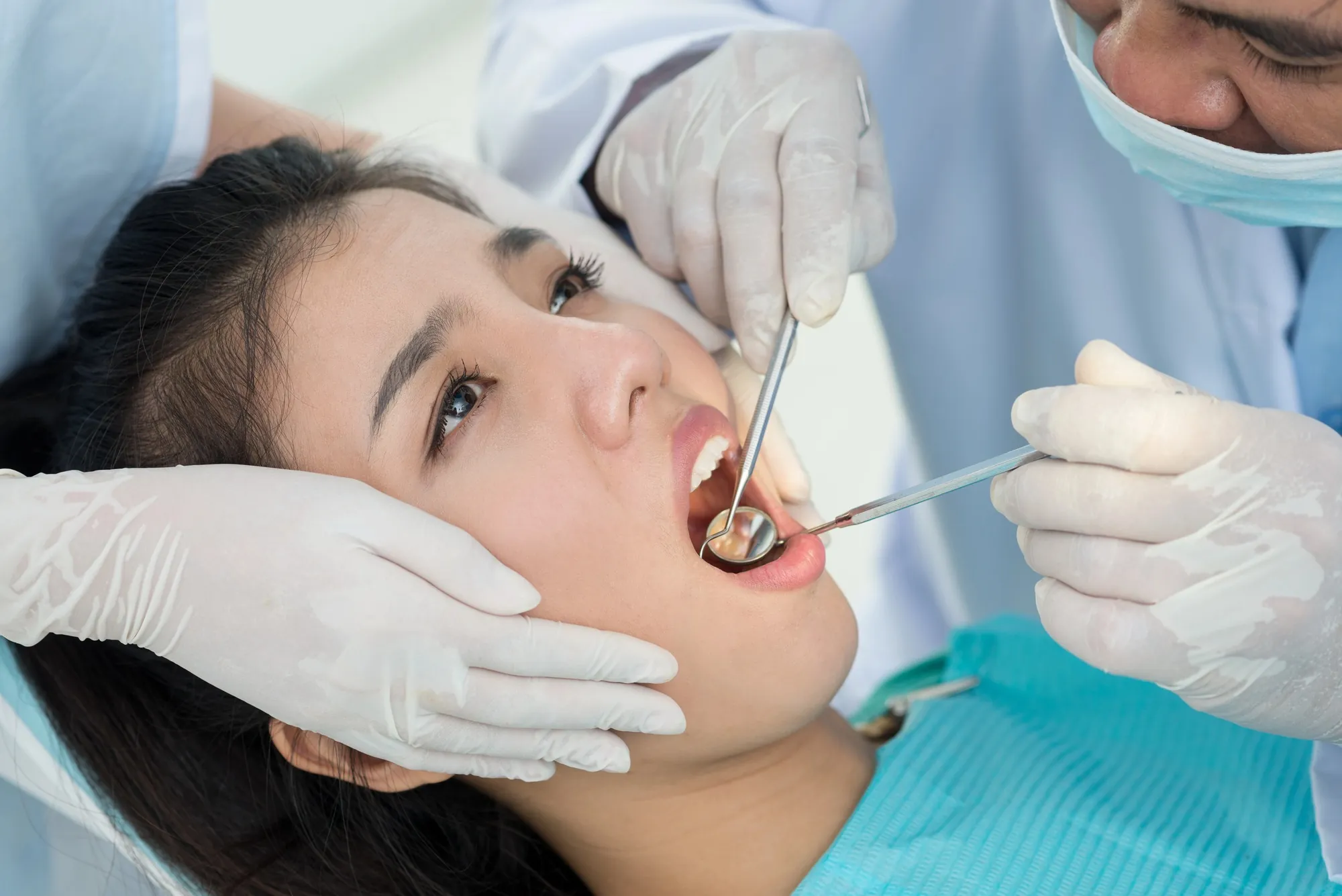 Dentist examining a patient’s teeth with a dental mirror during a same day crown appointment near Versailles, KY