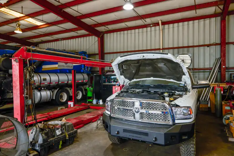 Cab-over heavy-duty truck tilted for engine service; open-hood pickup and trailer reading “FREE” surround tool-laden bay.
