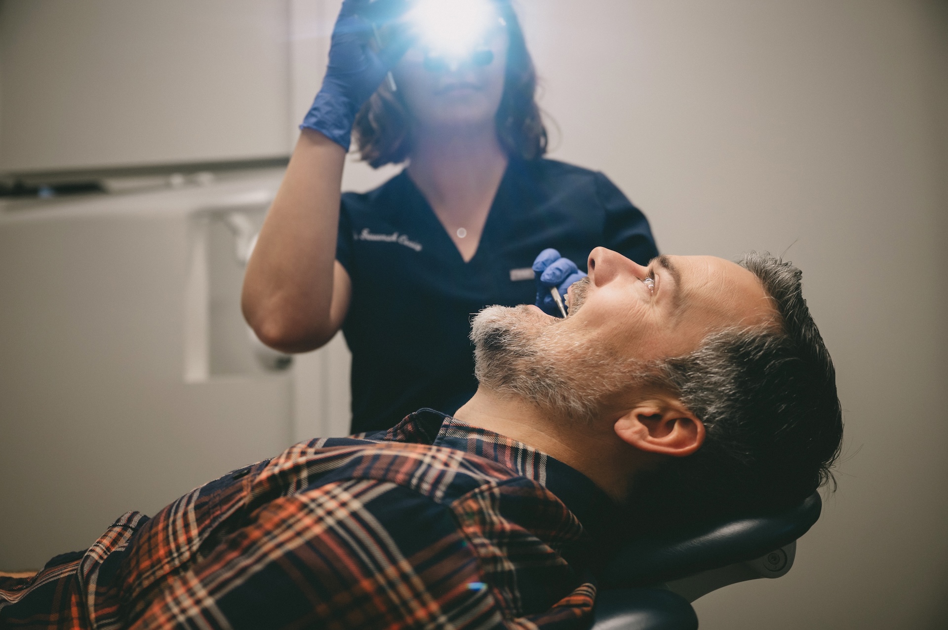 Dentist examines patient’s teeth under exam light in dental chair