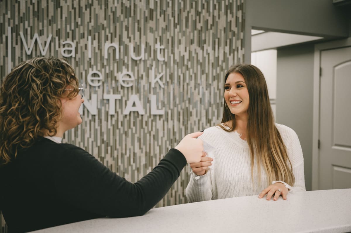Dental team member greeting a patient at the reception desk with a warm handshake
