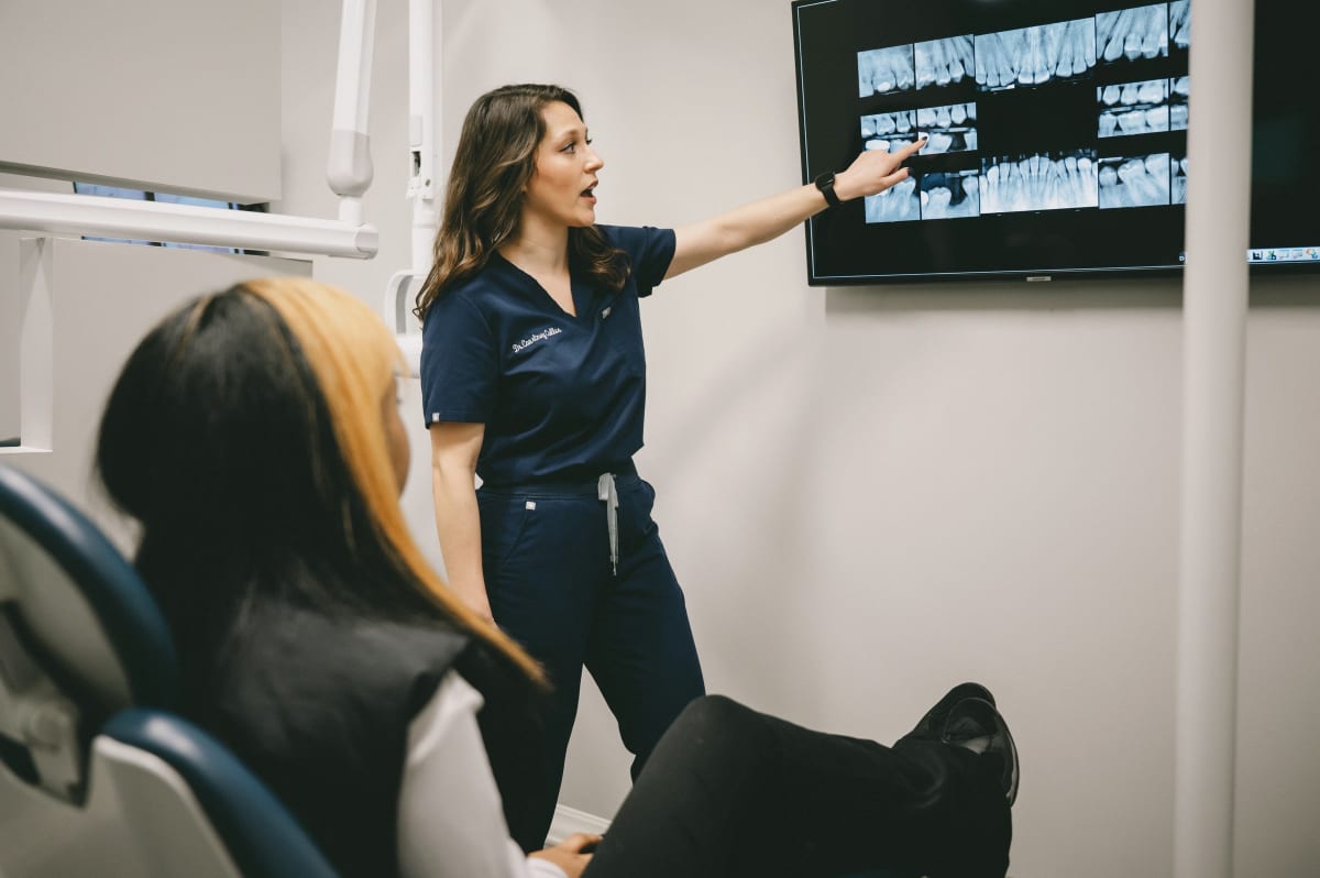 Dental professional pointing at digital display while consulting with patient in treatment chair