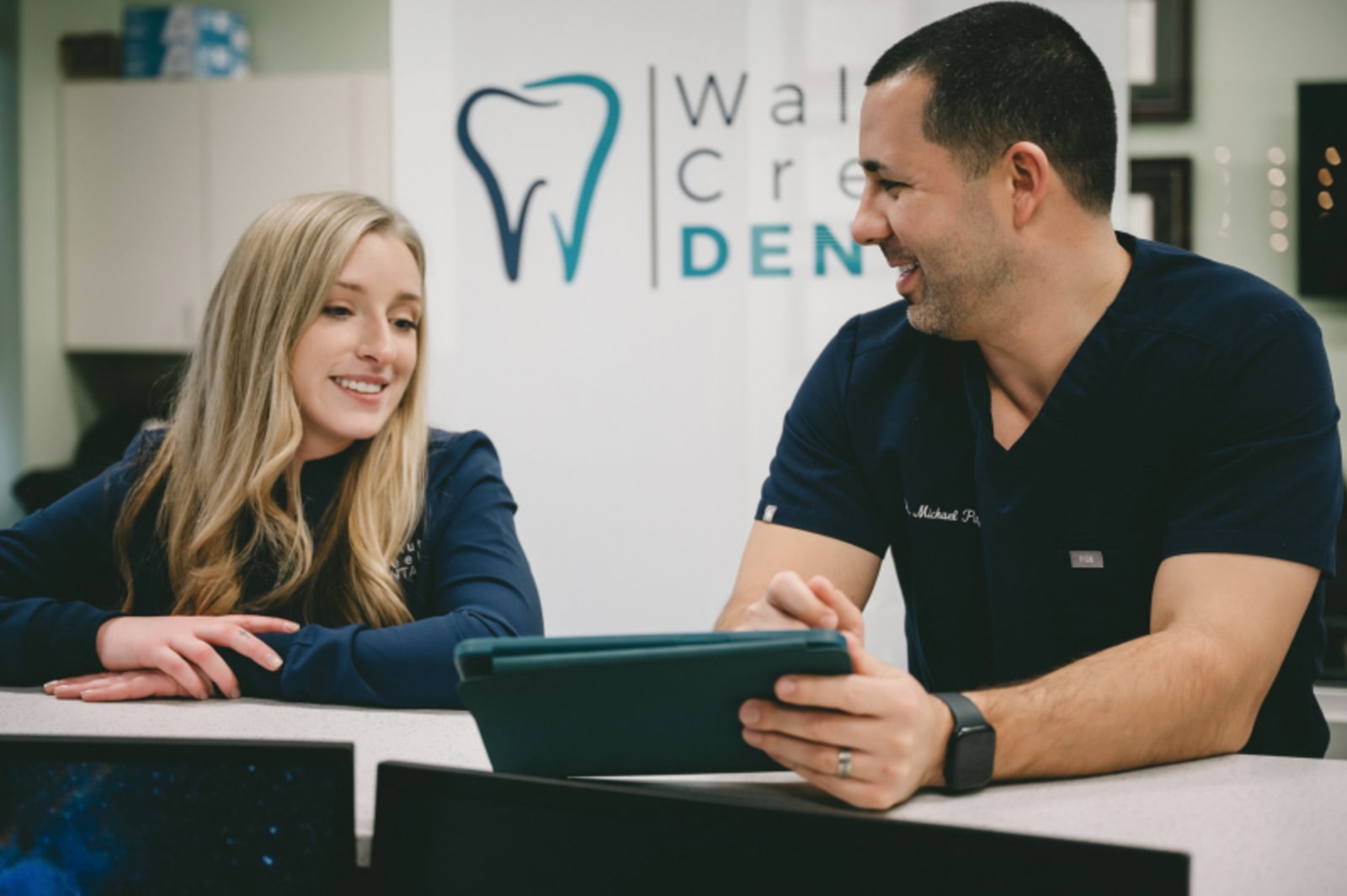 Female dentist in navy scrubs smiling at consultation desk in modern dental office